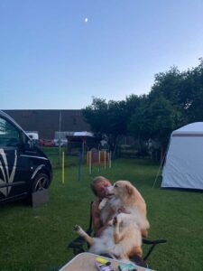 Hundehalterin im Campingstuhl bei Abenddämmerung mit großem Hund auf dem Schoß – entspannte Stimmung auf dem Hundeplatz