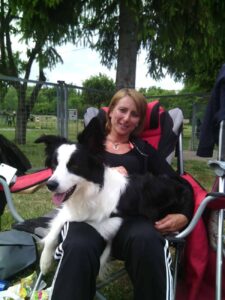 Hundehalterin sitzt mit Border Collie auf dem Schoß entspannt im Campingstuhl auf dem Hundeplatz
