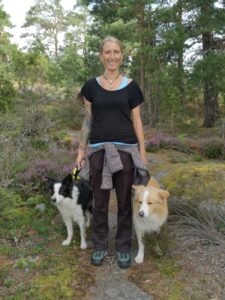 Hundehalterin mit zwei Border Collies bei einer Sommerwanderung im Wald – funktionale Kleidung und Outdoorschuhe im Einsatz
