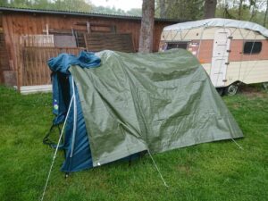 Improvisiertes Zelt mit Plane und Abspannseilen auf Wiese – Wetterschutz beim Campen mit Hund